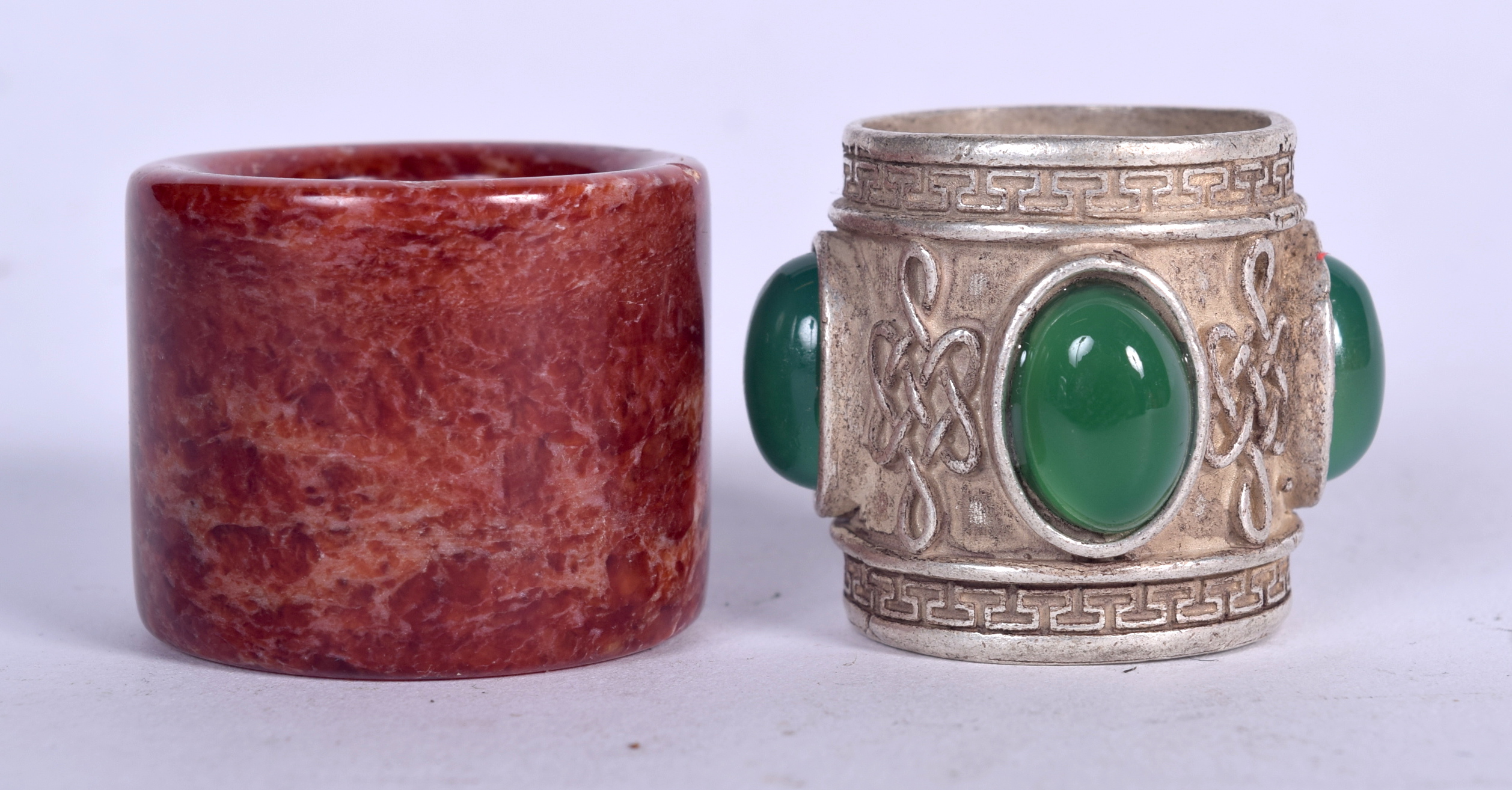 A CHINESE HARDSTONE ARCHERS RING, together with an apple jade inset white metal ring. (2)