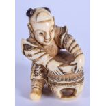 A 19TH CENTURY JAPANESE MEIJI PERIOD CARVED IVORY NETSUKE depicting a boy grasping a table. 4.5 cm x