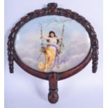 AN EARLY 20TH CENTURY EUROPEAN FAN SHAPED PORCELAIN PLAQUE painted with a female upon a floral swing