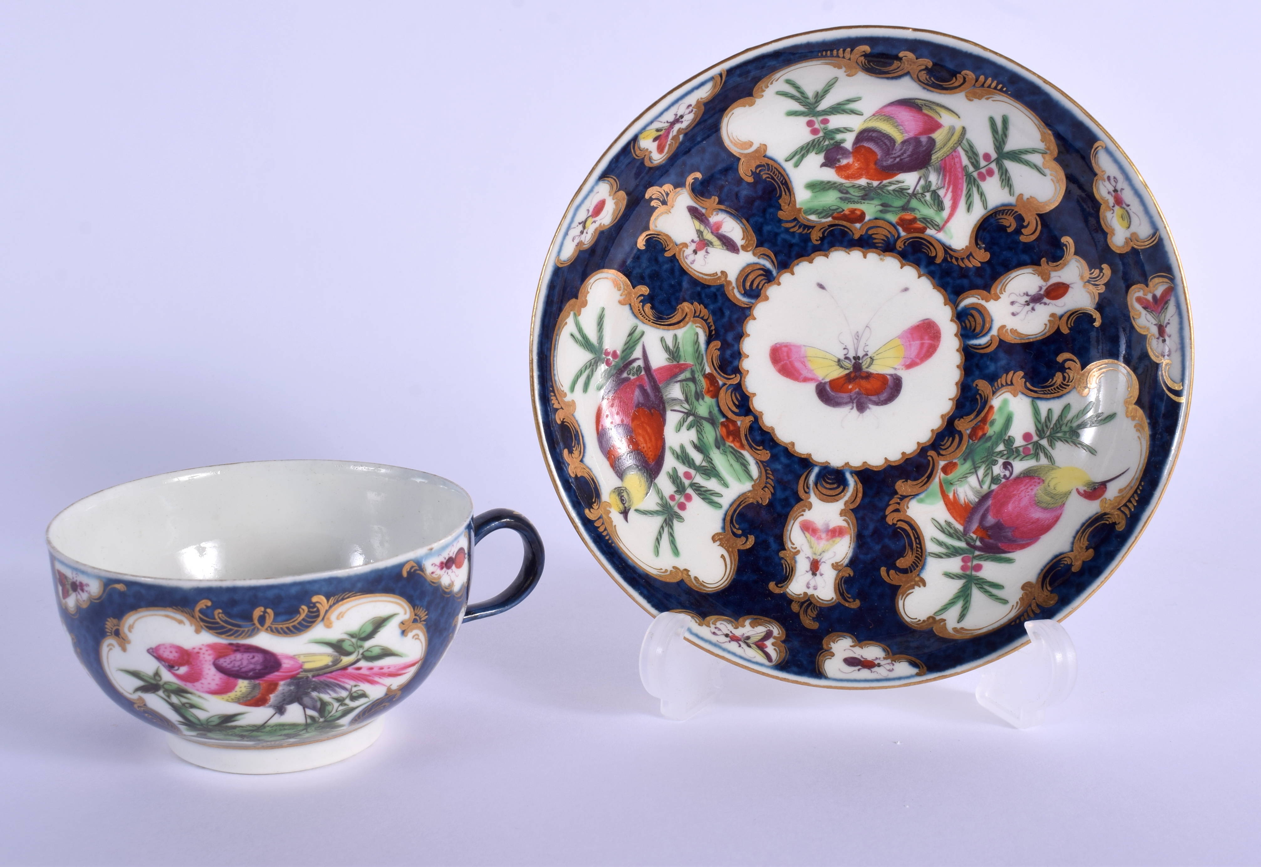 18th c. Worcester teacup and saucer painted with birds in a gilt mirror shaped panel on a blue scale