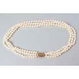 A CULTURED PEARL TRIPLE STRAND NECKLACE, the 9ct gold pierced flowerhead clasp set with seven