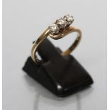A THREE STONE DIAMOND CROSSOVER RING, the round brilliants claw set to a plain 18ct gold shank,