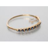 A SAPPHIRE AND DIAMOND STIFF HINGED BANGLE, the upper section grain set with nine oval facet cut