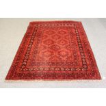 AN AFGHAN RUG, 20th century, the red field with repeating floral gul pattern in navy and ivory, navy