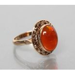 A COCKTAIL RING, the oval cabochon polished fire opal collet set to an open key border and a plain
