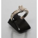 A DIAMOND RING, the baguette cut central stone of approximately 0.30cts claw set to shoulders each