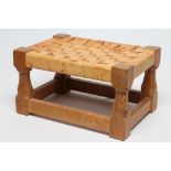 A ROBERT THOMPSON ADZED OAK FOOTSTOOL of oblong form with woven strap cow hide seat, raised on facet