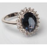 A SAPPHIRE AND DIAMOND CLUSTER RING, the oval facet cut sapphire of 2.91cts, claw set to a border of