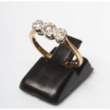A THREE STONE DIAMOND RING, the round brilliant cut stones illusion set to a plain shank, stamped