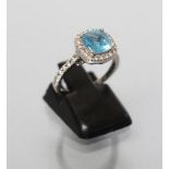 A DRESS RING, the cushion cut blue topaz point set to a border of numerous small diamonds to similar