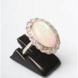AN OPAL AND DIAMOND CLUSTER DRESS RING, the oval cabochon polished pale opal open back collet set to