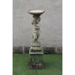 A COMPOSITE STONE BIRD BATH, the shallow basin issuing from a cornucopia held aloft by a putto, on