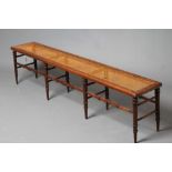 A VICTORIAN WALNUT(?) BENCH of rounded oblong form with caned seat, raised on eight ring turned