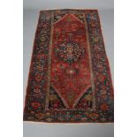 A PERSIAN TRIBAL RUG, the madder red floral field with navy blue hooked gul with tree at either end,