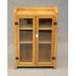 A PETER HEAP ADZED OAK BOOKCASE of shallow oblong form with a pair of glazed doors enclosing