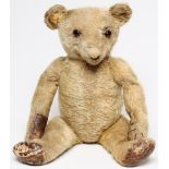 An English teddy bear, early 20th century, in worn gold plush, black/amber eyes, straw filled,