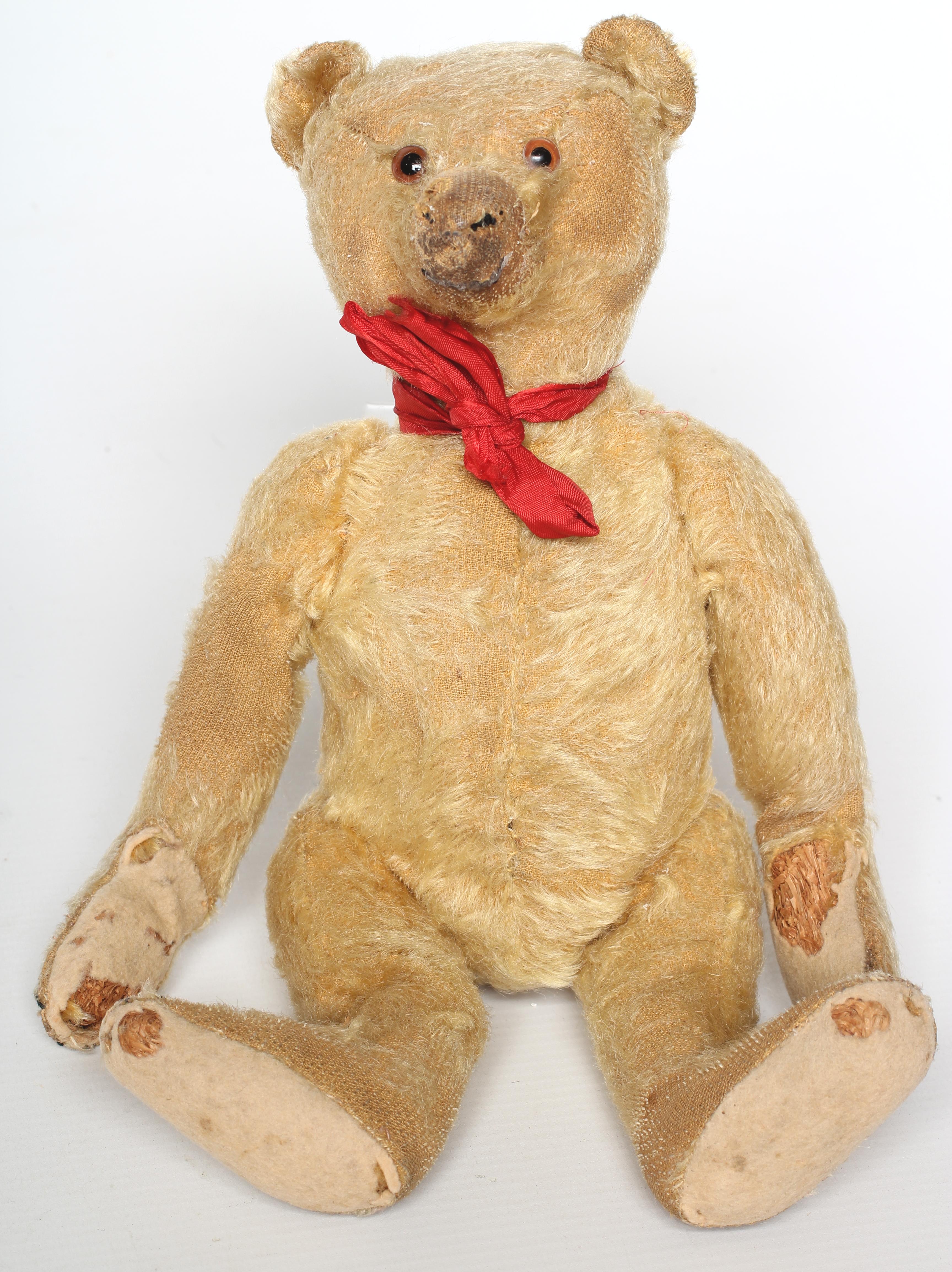 A Steiff teddy, c.1920, with glass eyes, felt pads, red bow and straw stuffing, 12" high (Est.