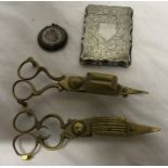 Two brass candle snuffers with a small silver compact and a plated card case.