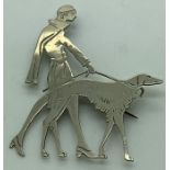 A white unmarked metal brooch in Art Deco style, a lady and her dog. 6 x 4cms.