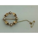 A 9ct gold and seed pearl brooch with safety chain formed as a circle of leaves and flowers heads.