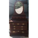 A 20thC mahogany chest of drawers with oval mirror to top.