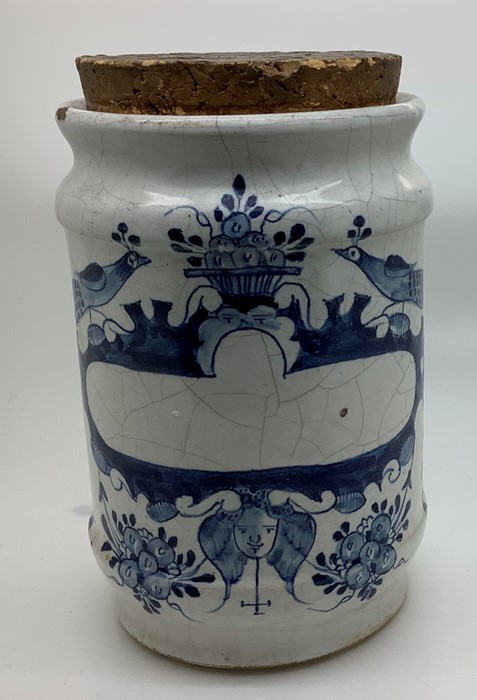 An 18thC Delft dry drug jar with cork stopper, peacocks flanking a basket of fruit with