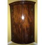 A mahogany double door bow fronted corner cupboard with string inlay. Three drawers to base of