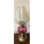A vintage brass and glass oil lamp with cranberry glass well, shade decorated with peacock feather