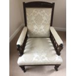 An Edwardian upholstered armchair on turned front legs and carving to crest rail.