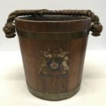 A wooden and brass fire bucket with rope handle and painted coats of arm to front. 40 l x 30.5 w x