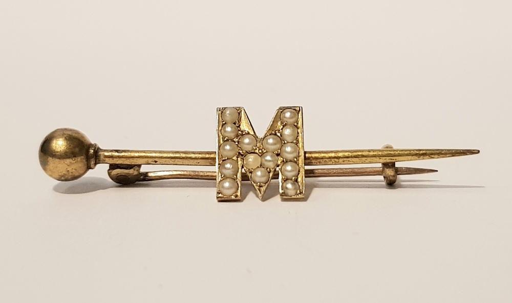 AN ANTIQUE 15CT BAR BROOCH SET WITH SEED PEARLS IN THE FORM OF THE LETTER 'M'