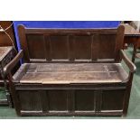 AN 18TH CENTURY OAK SETTLE, four panel, with lift up seat revealing storage within, having carved