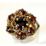 A 9CT YELLOW GOLD ORNATE 7 STONE GARNET CLUSTER RING, with decorative gold work between the