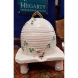 AN IRISH BELLEEK PORCELAIN HONEY POT with lift away lid, raised on tripod legs, 7" tall approx