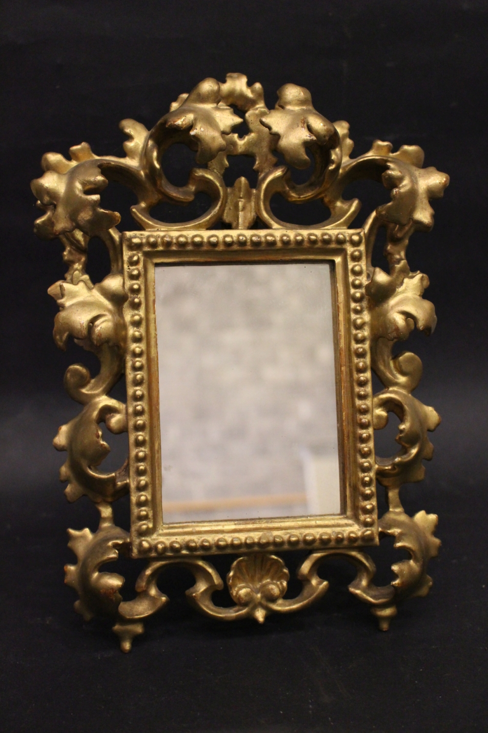 A TABLE TOP GILT FRAME / MIRROR, with raised foliage decoration, 12" x 8" approx frame