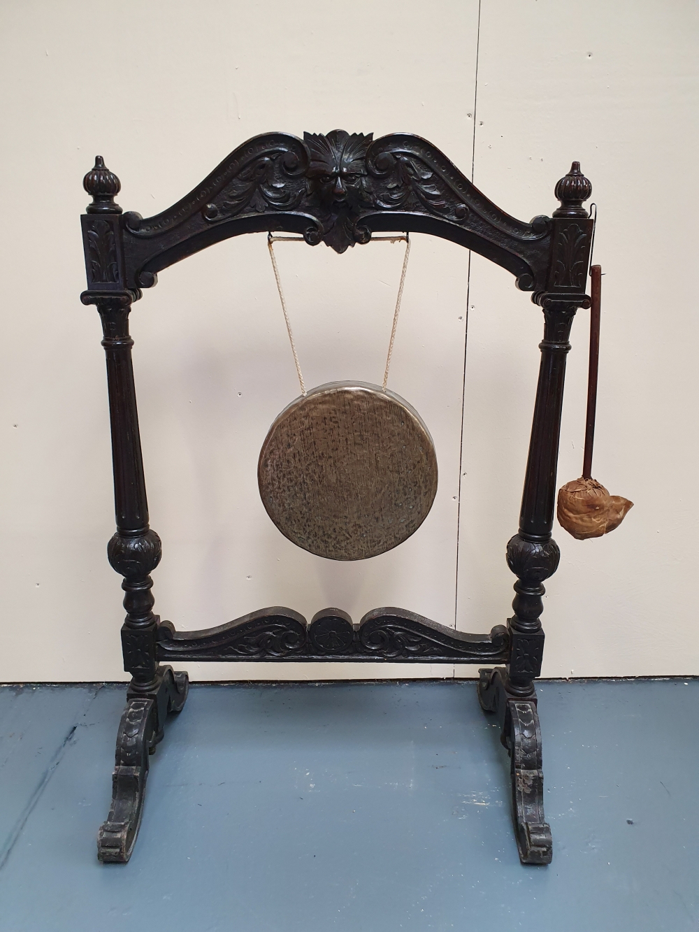 A 19TH CENTURY OAK FRAMED DINNER GONG - with carved mask head and brass gong, 48in x 32.25in x 21.