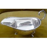 AN EARLY 20TH CENTURY SILVER SAUCE BOAT, with gadrooned rim, curved open handle, raised on tripod