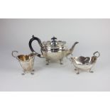 A George V silver three-piece tea set, oval faceted form with scroll borders, comprising teapot,