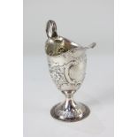 A George III silver cream jug, helmet shape with possibly later embossed floral & scroll decoration,