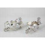 A pair of Continental novelty silver salts, in the form of cherubs pushing shell shaped barrows,