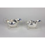 A pair of George V silver sauce boats with scallop borders and scroll handles, on three hoof feet,