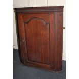 An oak hanging corner wall cupboard with carved frieze and panel door enclosing green painted