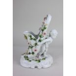 A Sitzendorf porcelain model of a putto supporting a slipper decorated with bocage roses, on