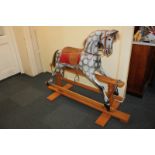 A large painted rocking horse in dapple grey, with leather saddle and bridle, horse hair mane and