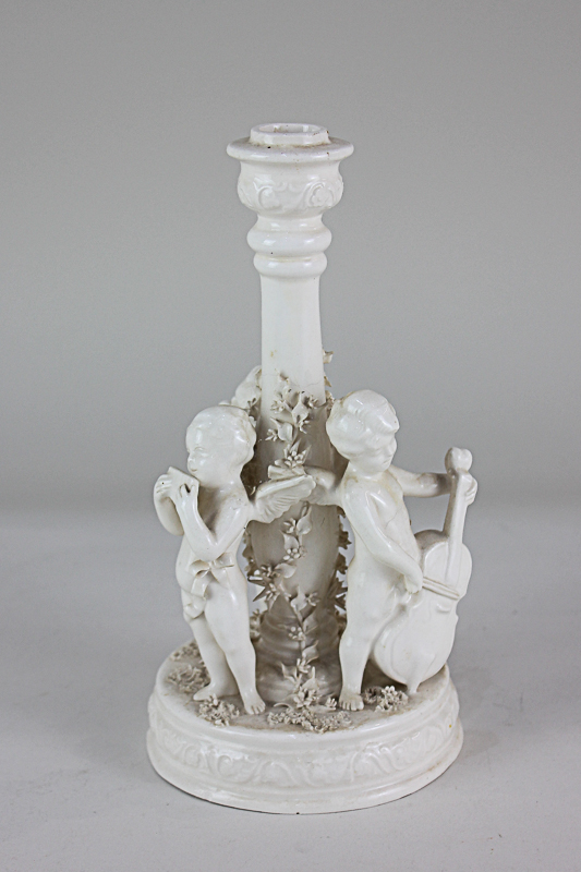 A blanc de chine candlestick with three winged cherubs playing musical instruments and floral bocage