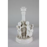 A blanc de chine candlestick with three winged cherubs playing musical instruments and floral bocage