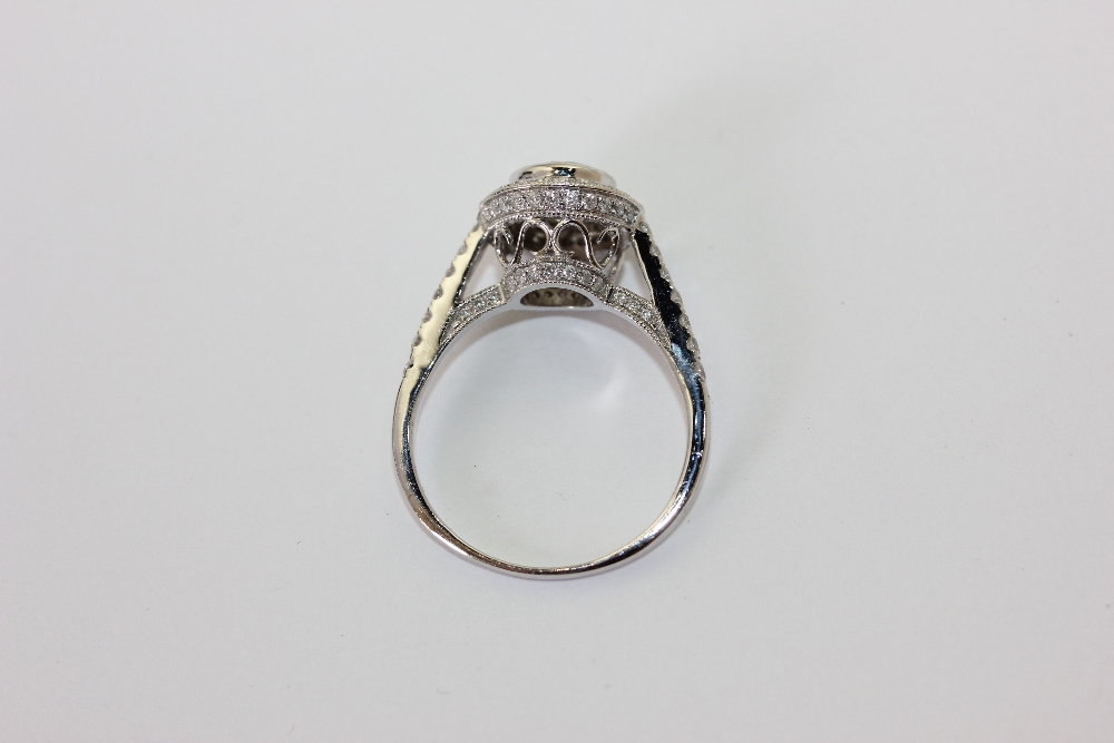 A diamond ring, the round brilliant cut stone set within a border of smaller stones, pave set - Image 2 of 2