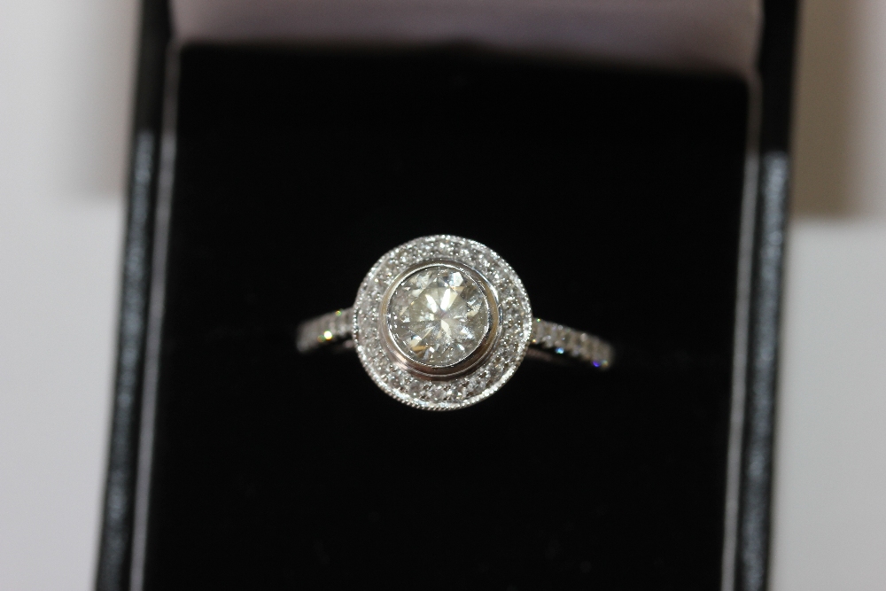 A diamond ring, the round brilliant cut stone set within a border of smaller stones, pave set