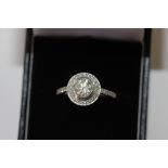 A diamond ring, the round brilliant cut stone set within a border of smaller stones, pave set