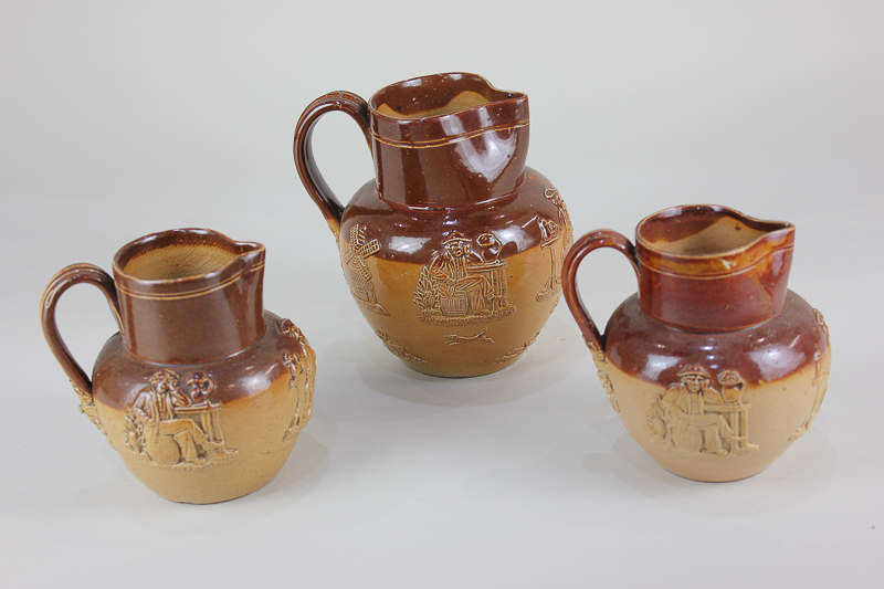 A collection of three Doulton Lambeth glazed brown stoneware jugs, decorated in raised relief with